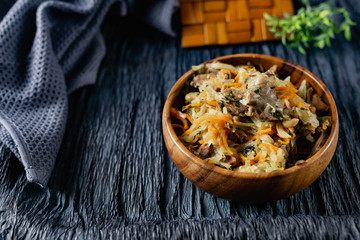 Stewed cabbage with oyster mushrooms and pork tongue with carrots and onions. Hot dish in a wooden...