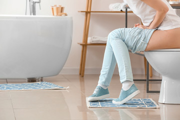Young woman with hemorrhoids sitting on toilet bowl in bathroom