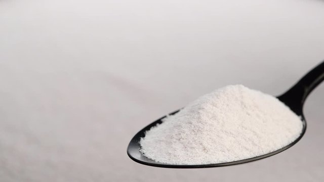 collagen powder in black spoon and collagen powder background rotating. Natural beauty and health supplement top view
