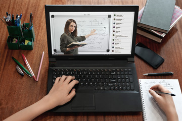 Student taking notes while watching online lesson at home during quarantine. Video conference with...
