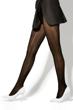 Cropped shot of female legs in ivory lacy fishnet tights with fancy jacquard pattern. The girl in a black satin skirt and white high heel shoes is striding on the white background. 