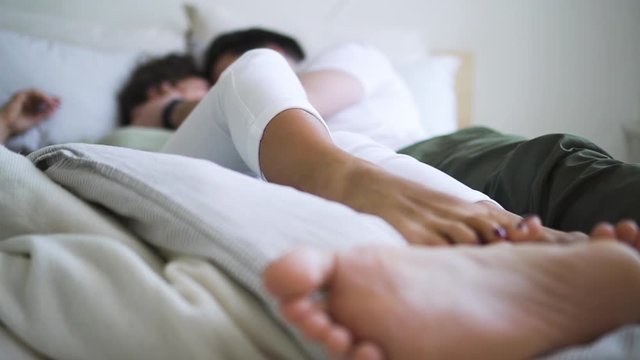 Young American couple is showing love and passion while lying on bed in white room spbd. Blurred view of pretty woman and bearded man have romantic time together, hugging and touching each other. Two