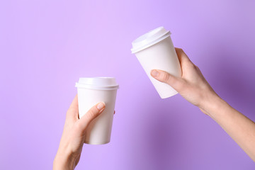 Hands with takeaway cups for drink on color background