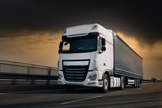 Semi-truck with cargo trailer driving at the hightway. Fast moving truck at the sunset