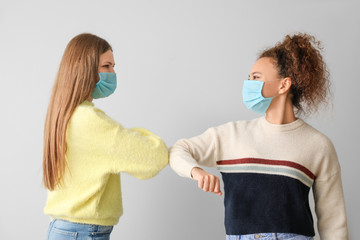 Young women in protective masks greeting each other on grey background. Concept of coronavirus epidemic