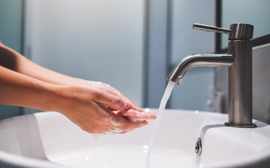 Woman cleaning and washing hands with soap under the faucet in bathroom