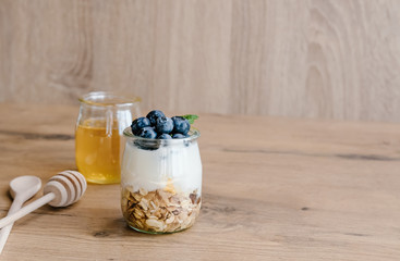 Healthy breakfast set with homemade yogurt with granola and blueberries and honey on wooden background.