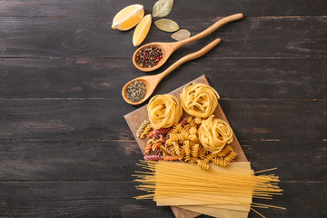 Different uncooked pasta with spices on wooden background