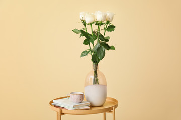 Vase with beautiful roses and cup of coffee on table