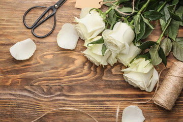 Beautiful white roses, thread and scissors on wooden background