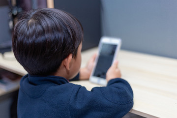 A boy sitting using a smartphone on a desk to study