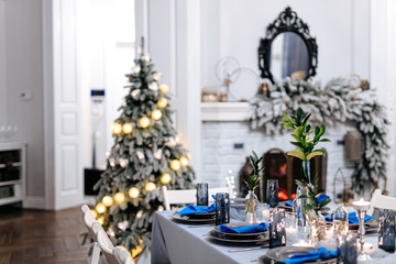 White living room with fireplace, christmas tree and long table  with stylish serving. Decoration details for celebration.