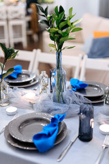 Close up of decorative details on table made with blue napkins, candles and green leaves. Festive table with trendy serving. Concept of event and celebration.
