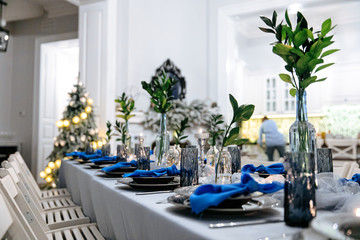 Decorated table for celebration with candles and green leaves. Beautiful serving in trendy white and blue colors. Concept of exclusive event.