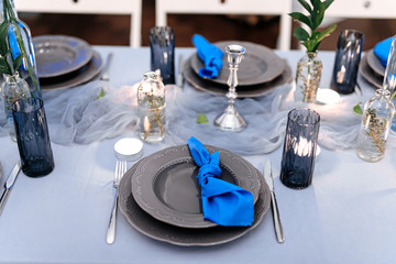 Close up of festive table served with plates, cutlery and glasses decorated with candles and green leaves. Decoration details and celebration concept.