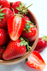 Close up view of freshly picked ripe natural organic strawberry fruits in a wooden bowl on a white background.