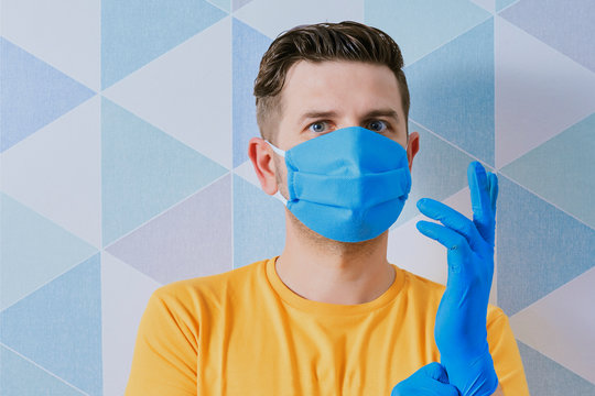 white man on a blue background with a protective mask wearing nitrile gloves