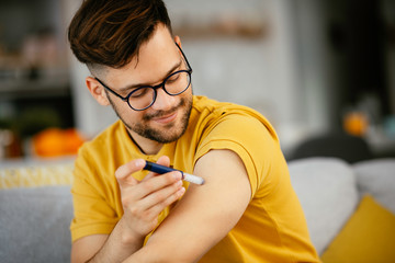 Young man giving himself an insulin shot at home
 - obrazy, fototapety, plakaty