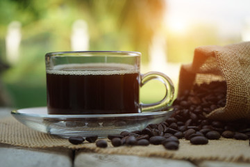 Hot Coffee cup and coffee beans roating on the wooden table beside green garden ranges in the morning sunrise