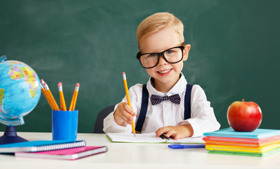 funny child   schoolboy  boy student sitting at   table near  school blackboard.