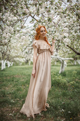 red-haired girl in a beige dress in the garden