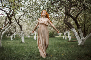 red-haired girl in a beige dress in the garden
