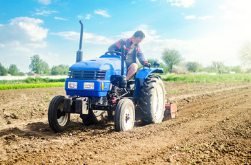 Obraz premium Farmer on a tractor with milling machine loosens, grinds and mixes soil. Loosening the surface, cultivating the land for further planting. Farming and agriculture. Cultivation technology equipment