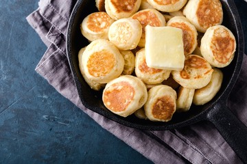 Mini cereal pancakes in cast iron frying pan on grey napkin, blueberry. Dark blue cement background, top view, close up