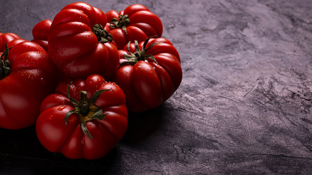 in the foreground, on a textured black background, some ripe and fresh tomatoes covered with drops of water. Copy space