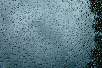 Wet window glass with raindrops and reflection of cloudy sky outdoors. Abstract background and...