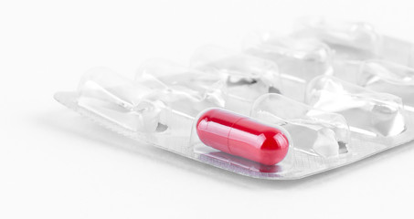 Closeup of one red pill in a blister pack on white background
