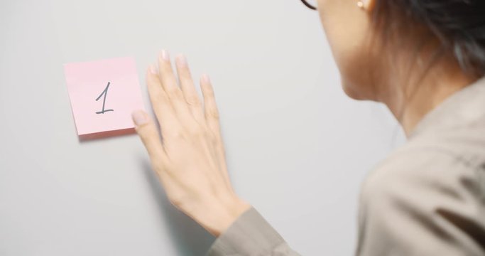 Young woman sticking pink reminder stickers with numbers 1 2 3 on a gray board. Copy space