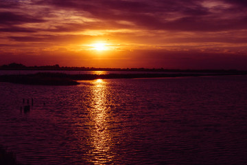 Saline di Cervia Natural Park and Wildlife Reserve at sunset, a wildlife and bird sanctuary, perfect for birdwatching. Sun going down above water with rays reflections.