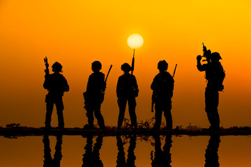 The military silhouettes of soldiers hold gun against with sunset sky background.