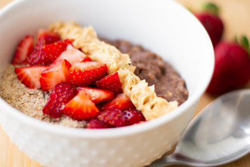 Chocolate cocoa oatmeal with almond meal, chopped strawberries and creamy peanut butter on a wooden surface. Strawberry, almonds, napkin and spoon in the background