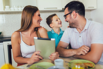 Happy family having breakfast together at home in the kitchen, and using digital tablet.