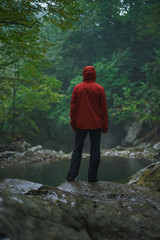 Hiker from behind standing in mountains in rain with backpack wearing raincoat.