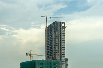 Building under construction, Condo construction, Building site with yellow cranes, and blue sky background.