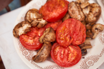 Vegetables for grilling tomatoes and mushrooms on a white plate