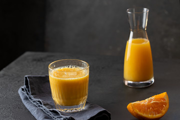 Orange juice glass and oragen juice bottle on dark background. Refreshment  fruit beverage.