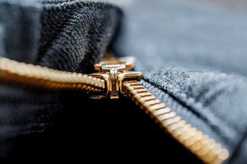 Close up image of a black denim jeans with its metal zipper or fly open and zipper tape metallic puller, bridge, slider body and chain visible along with brown stitching