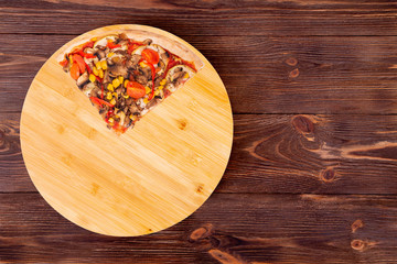 A quarter of pizza with mushrooms, corn, cherry tomatos, courgettes and bell peppers on a round platter which is on wooden rustic background, top view and copy space