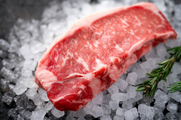 Raw fresh New York beef steak on ice with herbs and rosemary, close up