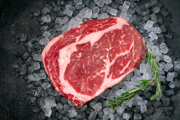 Raw fresh Rib eye beef steak on ice with herbs and rosemary, top view