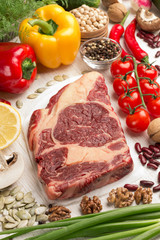 Raw meat. Marbled beef steak. Green onions, chili peppers, greens, walnuts, on table.