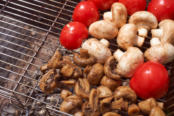 vegetables for grilling tomatoes and mushrooms mushrooms lie on the grill, which stands on a grill with coals