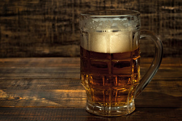A glass of amber beer. Glasses on a wooden table. Black shabby boards on the background. Bright...