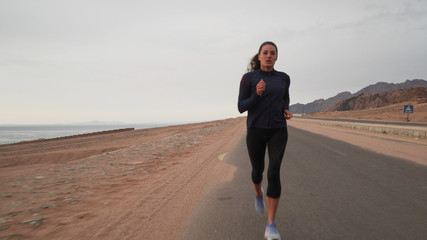 Front view of brunette caucasian woman jogging along the road at seashore