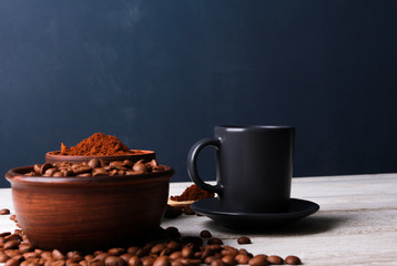 Espresso cup, roasted Arabica beans in clay bowls, coffee powder on while table against dark blue wall. Side view, copy space. Coffee shop, morning, baristas workplace concept