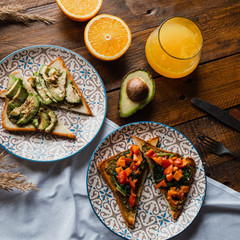 Avocado and spinach toasts with red bell pepper, fresh squeezed orange juice on dark wooden board. Vegetarian food, healthy diet concept.